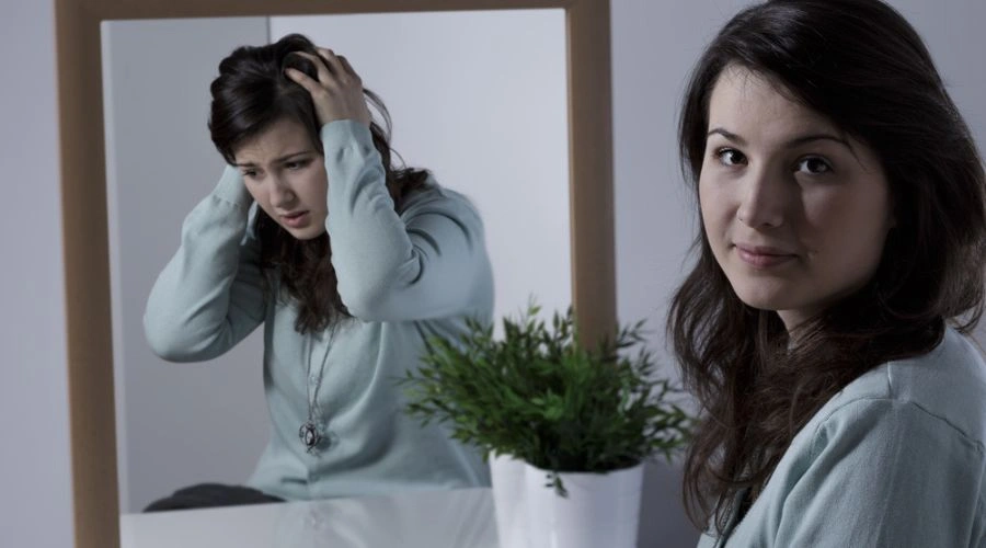 Female looking in mirror holding hands on head on mirror image and looking at camera at other end - displaying Common Symptoms of BPD