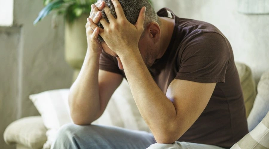 Man looking down holding hands on his head displaying the Consequences of Nervous System Dysregulation