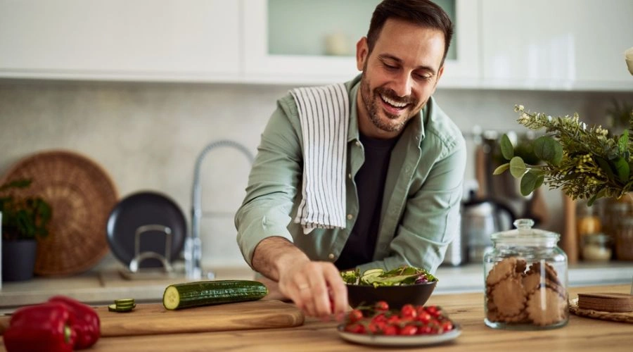 Content man in kitchen picking a grape tomato with other healthy vegetables around - Creating a Healthy Mindset