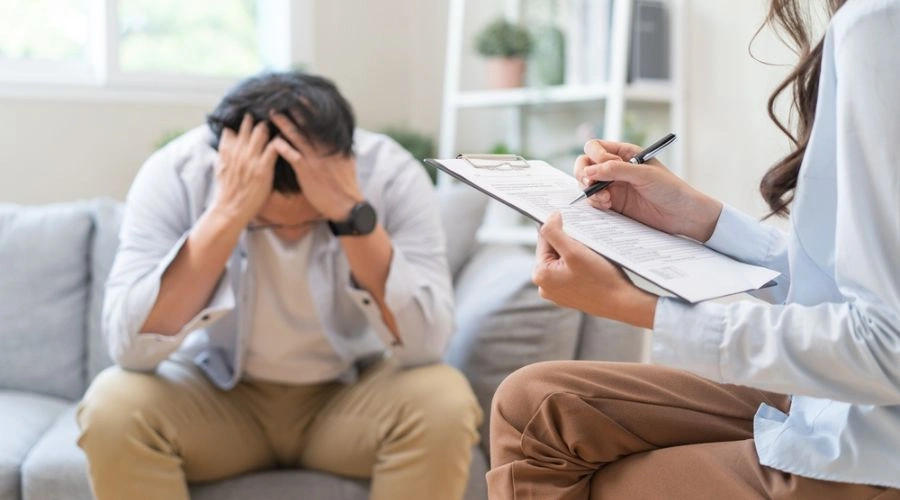 Man in therapy sitting on sofa holding hands in his hair displaying Treatment Options for Trauma