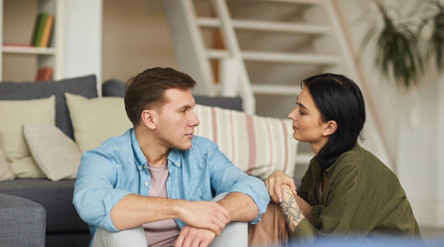 Image of a male and female sitting in front of a sofa and looking at each other