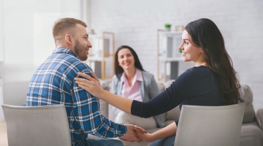 Image of a smiling male and female in therapy as a smiling counselor looks on