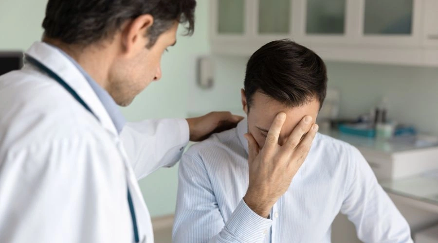 Image of a male doctor talking to a distraught male patient who is holding is hand on his face