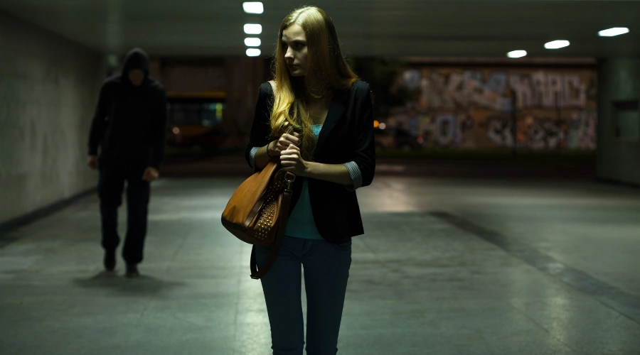 Image of a female walking alone in a parking lot clutching her shoulder bag as a man follows behind her