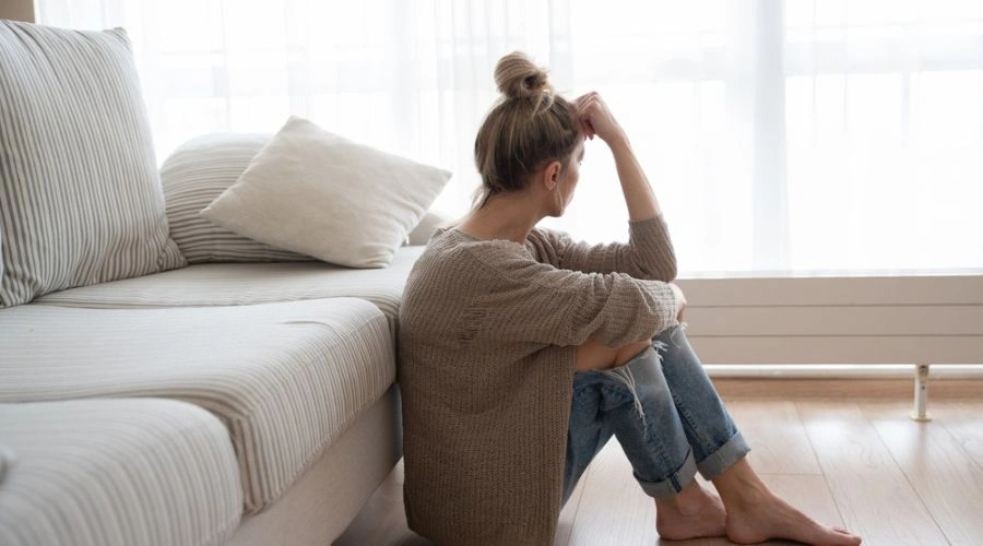 Image of a woman sitting alone on the floor in front of a sofa - Injustice Trauma - Catalina Behavioral Health
