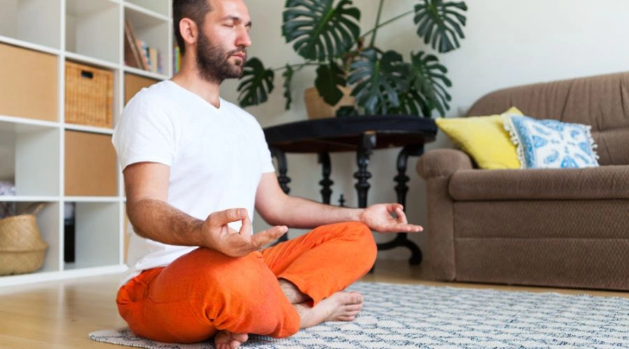 Man sitting on a rug in his living room,  practicing yoga and meditation 