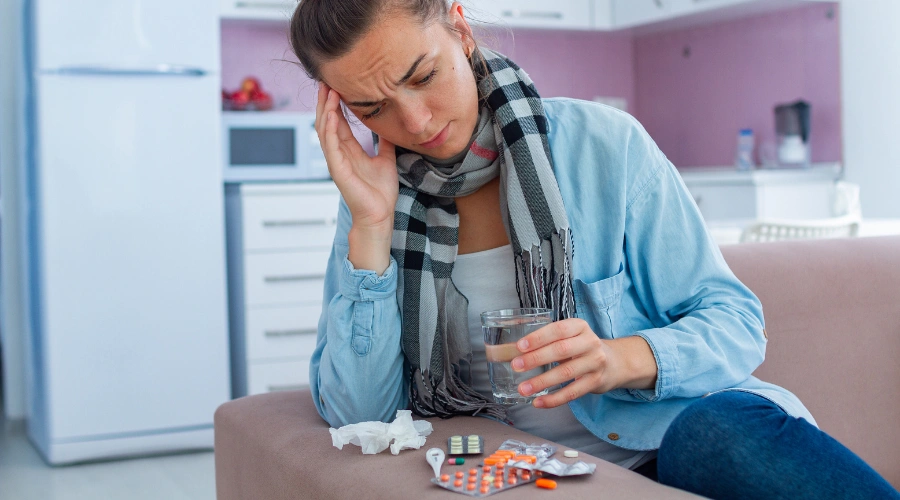 Image of woman sitting on a sofa and holding a glass of water, beside a wide array of Benzodiazepine pills on the sofa arm - Benzodiazepine Induced Neurological Dysfunction - Catalina Behavioral Health