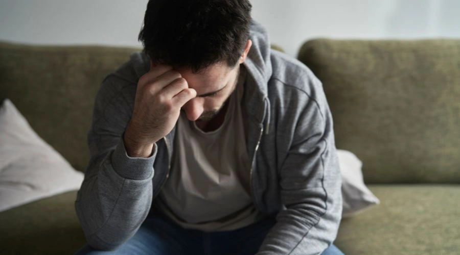 Image of a man sitting alone on a sofa with his hand on his head - Can Psychosis Be Permanent - Catalina Behavioral Health