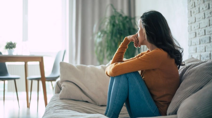 Image of a woman in despair, sitting alone on a sofa, staring at the window - What Is An Emotional Shutdown - Catalina Behavioral Health