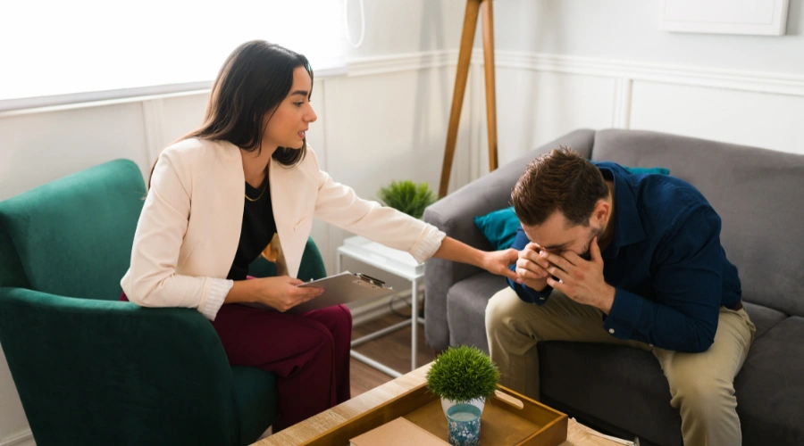 Image of a man sitting in therapy with his hands covering his face, as his counselor tries to console him - Treatment for Dependent Personality Disorder - Catalina Behavioral Health